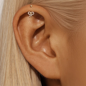 Detailopname van gouden strikvormige helix piercing met fonkelende zirkonia steentjes