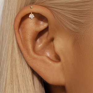 Macro-opname van een gouden helix-piercing met drie waaiervormige zirkonia's op het oor