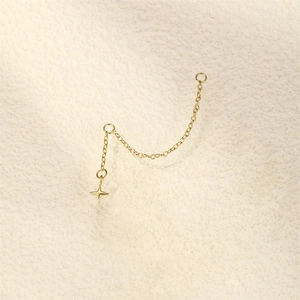 Macro shot of gold-plated chain earring with star pendant on a textured cream surface