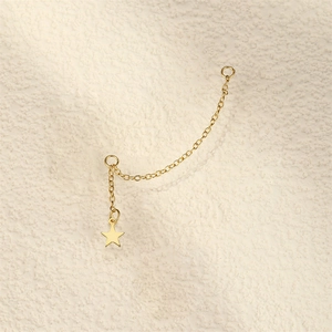 Macro detail of gold star pendant earrings with a long chain and minimalist design