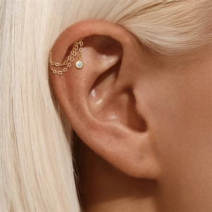 Close-up of gold double chain helix earring with round zircon on a model's ear