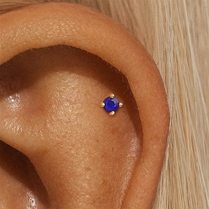Macro view of blue lapis lazuli stud earring with gold four-prong setting on ear