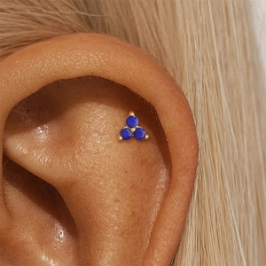 Macro view of a gold clover stud earring with three blue lapis lazuli stones on ear