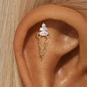 Makroansicht von Piercing-Schmuck aus Gold mit Zirkonia und Kette an der Ohrmuschel