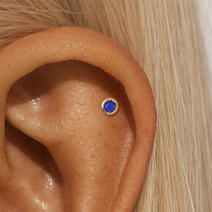Macro shot of gold-plated lapis lazuli stud earring worn on the ear cartilage