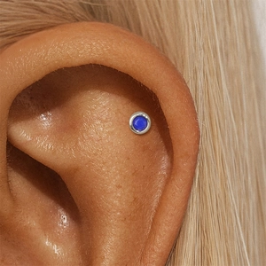 Macro view of a faceted blue lapis lazuli stud earring worn on the ear cartilage