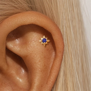 Macro view of a gold starburst cartilage stud earring with a blue lapis lazuli stone