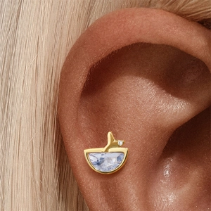 Detailopname van een gouden walvisstaart oorknopje met een lichtblauwe edelsteen en diamant