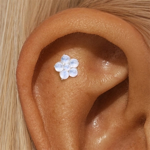 Close-up of a silver floral moonstone stud earring worn on the cartilage ear piercing