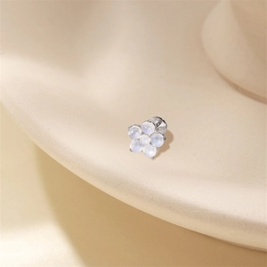 Macro shot of silver flower moonstone stud earring on a warm beige ceramic display tray