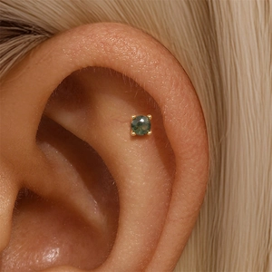 Macro shot of s925 gold-plated green moss agate stud earring worn on the ear cartilage