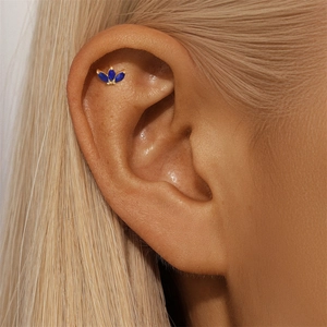 Macro shot of a gold clover cartilage stud earring with inlaid blue lapis lazuli stones