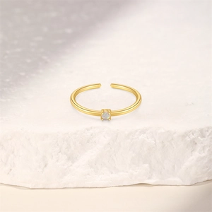 Detail of adjustable gold ring featuring a four-prong set round opal on a stone surface