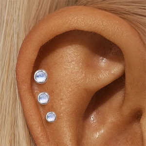 Macro detail of three graduated bezel-set moonstone stud earrings in silver on ear
