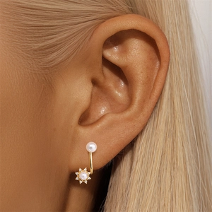 Detailed view of U-shaped gold pearl earrings with a sunflower pendant on ear