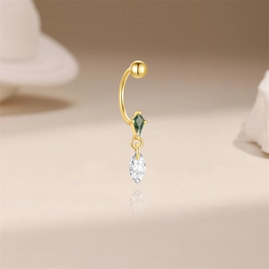Macro detail of gold curved barbell piercing with green diamond and marquise stone