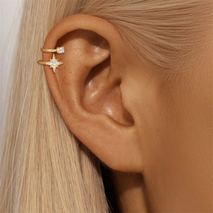 Dettaglio di ear cuff dorati con zircone quadrato e ciondolo a stella su orecchio