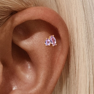 Close-up of golden piercing earring with teardrop and marquise purple gemstones