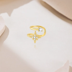 Dettaglio di ear cuff a stella a otto punte dorata con zirconi bianchi su sfondo neutro