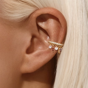 Dettaglio di ear cuff dorato con zirconi marquise e pendenti floreali rossi