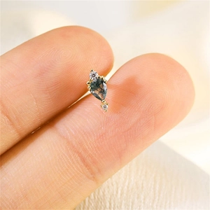 Detailed close-up of a tiny teardrop moss agate stud earring held between fingers