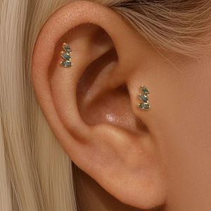 Close-up of gold ear studs with green stones worn on cartilage for a stylish look