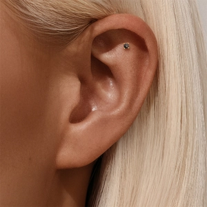 Close-up of s925 silver helix piercing with black round gemstone in four-prong gold setting