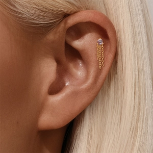 Detail van S925 zilveren helix piercing met opaalsteen en gouden kettingkwastjes