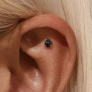 Macro shot of gold claw-set black rutilated quartz stud earring on upper ear cartilage