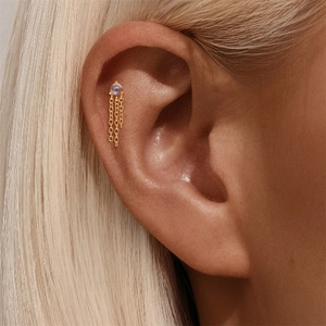 Macro-detail van gouden kwastje kraakbeenpiercing met opaal kraal en hangende kettinkjes