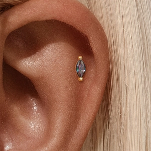 Macro-opname van een goudkleurige oorknop met marquise aurora-steen op het kraakbeen
