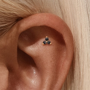Macro detail of s925 silver ear stud featuring three black gems in gold claw settings