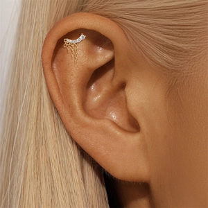 Close-up of a s925 silver ear stud with curved clear zircons and flowing gold tassels