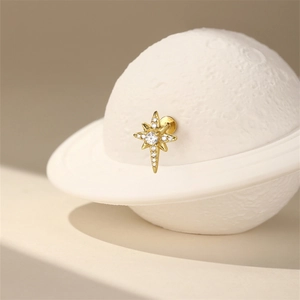 Detail of a golden starburst piercing stud with zircon on a miniature planet display