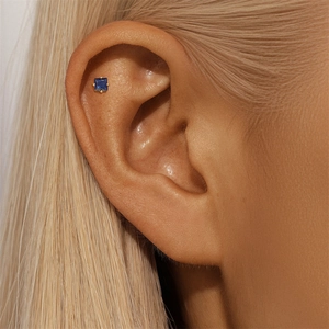 Close-up of square blue zircon earring in gold setting worn on ear cartilage detail