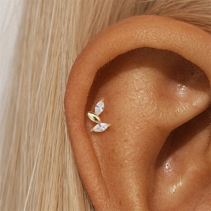 Close-up of golden leaf cartilage stud earring with cubic zirconia on a model's ear