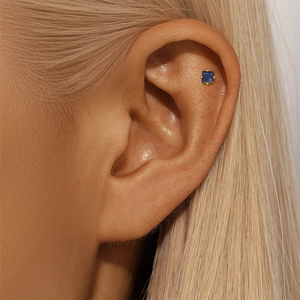 Detailed close-up of a blue square zircon stud earring with a gold four-prong setting