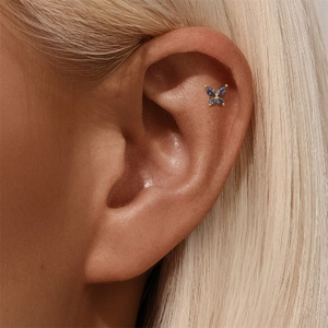 Detailopname van een vergulde vlinder helix piercing met gekleurde edelstenen op het oor
