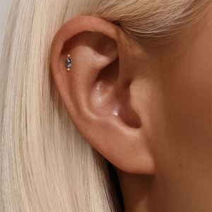 Macro view of a marquise-cut charcoal gem earring in gold setting on the ear