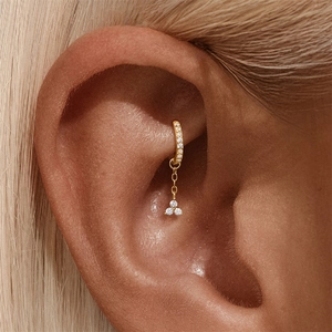 Primo piano di un ear cuff dorato con pavé di pietre e pendente triangolare a tre diamanti
