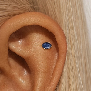 Detail of oval blue zircon stud earring in gold setting worn as a conch piercing