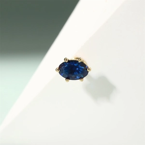 Macro shot of oval blue zircon earring with a six-prong gold setting on silver