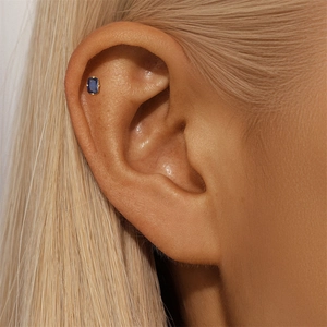 Close-up of a square sapphire blue zircon stud earring set in gold on a model ear