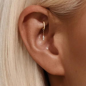 Dettaglio di piercing conch dorato con cerchio di zirconi e catena a tre pietre