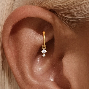Dettaglio di orecchino conch dorato con due zirconi cubici indossato dal modello