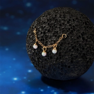 Detail of s925 silver golden chain with three opal beads on volcanic rock and starry background