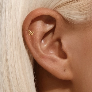 Detail shot of a delicate gold butterfly cartilage stud earring on a human model