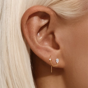 Macro shot of gold tassel flower earring with dangling pear-cut zircon stone on ear