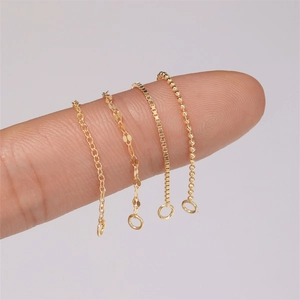 Macro shot of four delicate gold-plated silver chain styles held by fingers for size reference