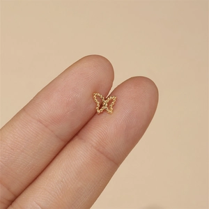 Close-up of a tiny gold butterfly cartilage stud earring held on a fingertip